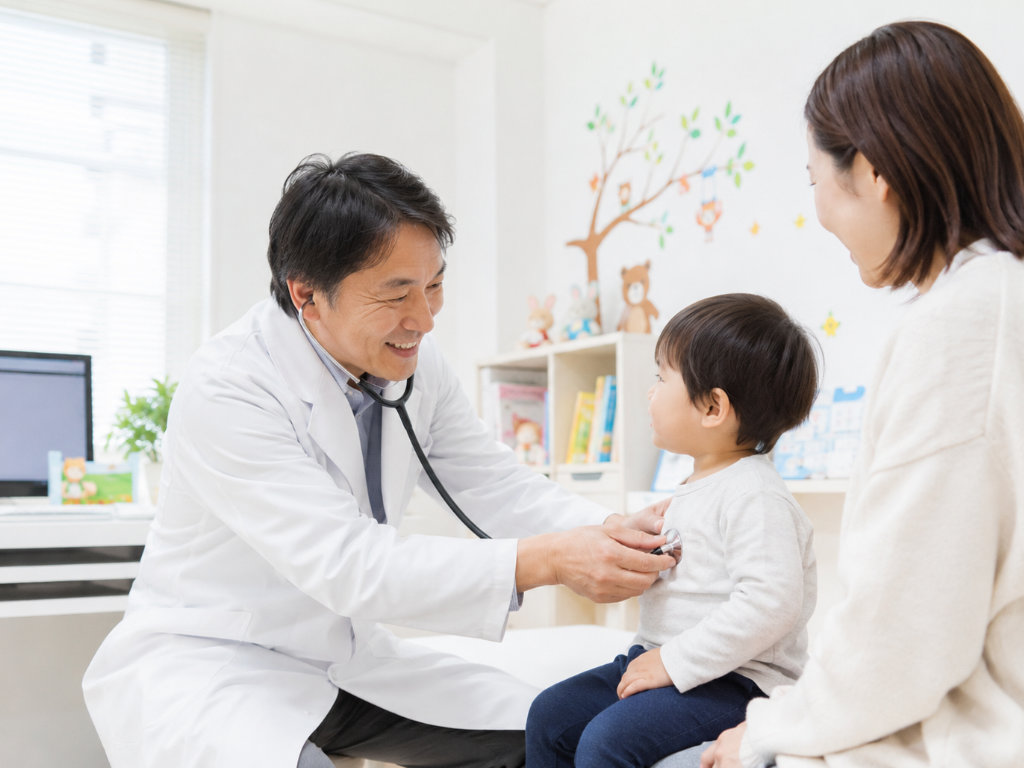 小児科で医師が子どもに聴診し、保護者が見守っている診察室の写真